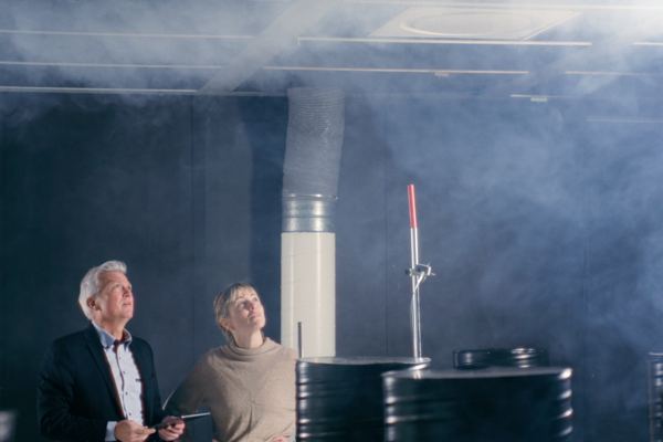 People in a lab environment looking at air diffusor in the ceiling while doing a smoke test to look at the air diffusion in the room